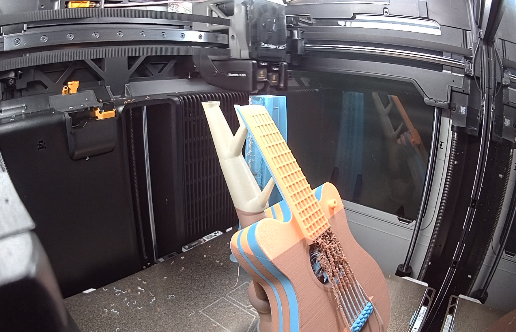 A multicolor 3D-printed guitar prototype inside a fabrication machine.